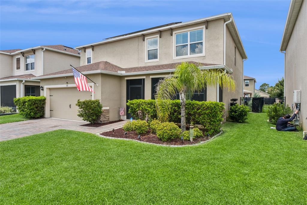 A two-story tan stucco house with a garage, a front lawn, and a palm tree — 358 LAZIO CIRCLE, DEBARY, FL