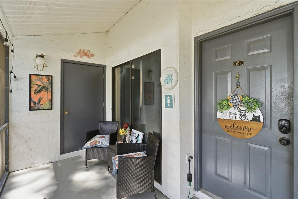 A covered entryway features two wicker chairs, a gray front door, and decorative wall art — 174 WATERFALL WAY UNIT 101, ALTAMONTE SPRINGS, FL