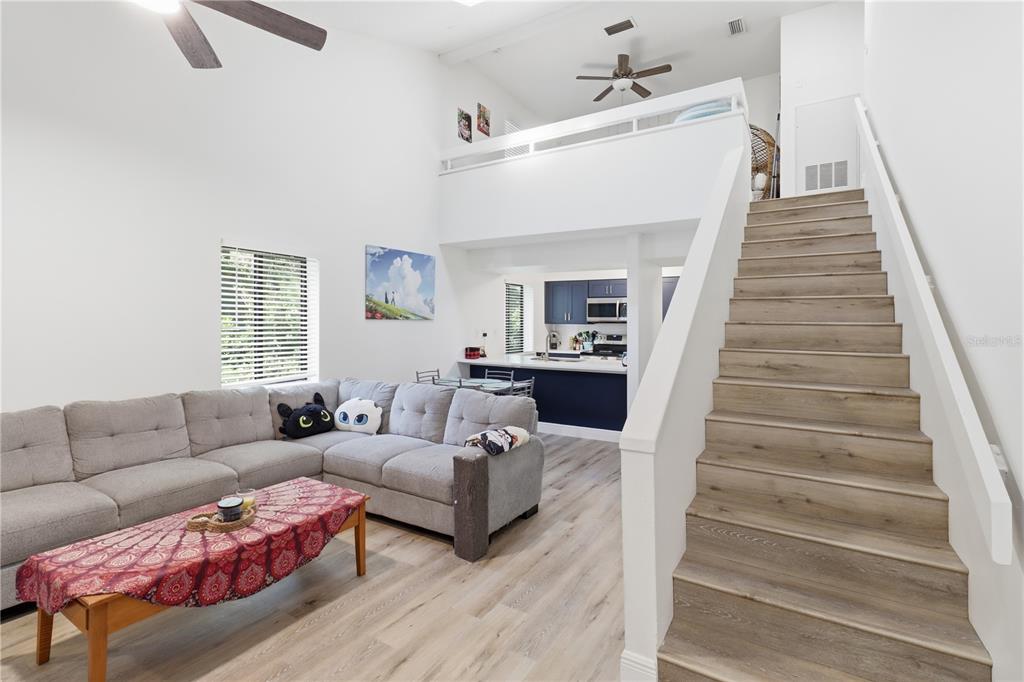 A living room with a sectional sofa, wooden stairs, and an open loft area above — 174 WATERFALL WAY UNIT 101, ALTAMONTE SPRINGS, FL