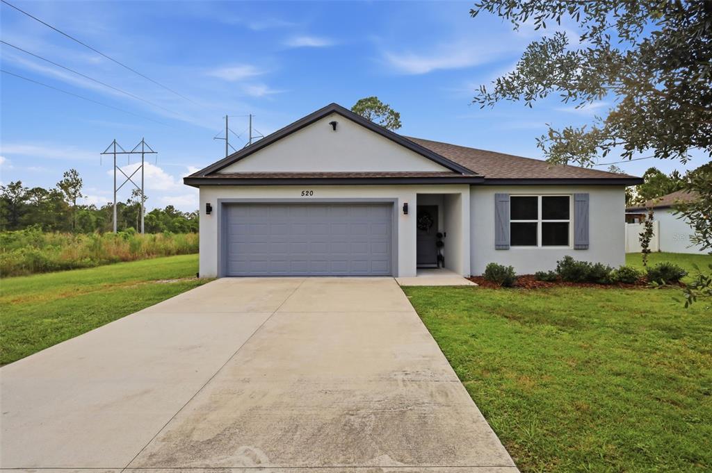 A single-story house with a gray garage door, light-colored stucco exterior, and a concrete driveway — 520 S SHELL ROAD, DELAND, FL