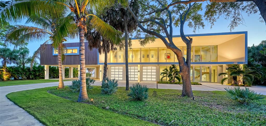 A modern two-story home on stilts features a wood-paneled upper level and glass garage doors — 4123 BAY SHORE ROAD, SARASOTA, FL