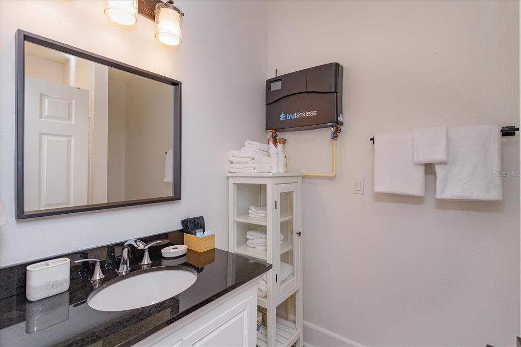 A bathroom features a black granite vanity, a wall-mounted tankless water heater, and white cabinetry — 1802 CHAMBERLIN STREET, ORLANDO, FL