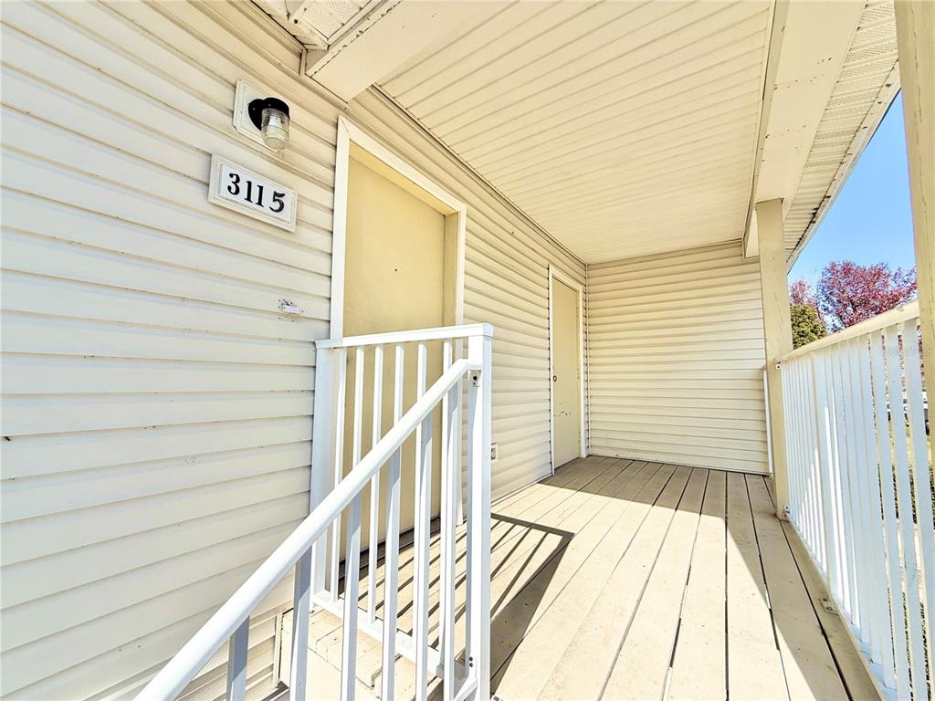 A covered wooden porch features white siding, a railing, and two beige entry doors — 3115 FOX SQUIRREL DRIVE UNIT 3115, KISSIMMEE, FL