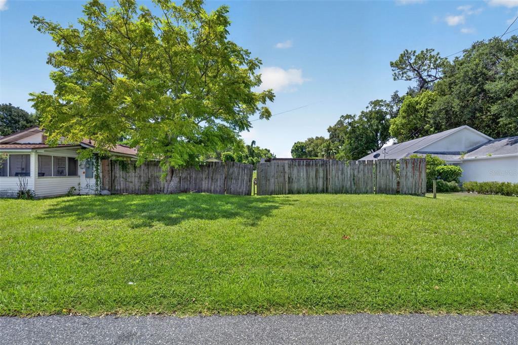 A grassy vacant lot sits between two houses, separated by a weathered wooden fence — NEUSE AVENUE, ORLANDO, FL