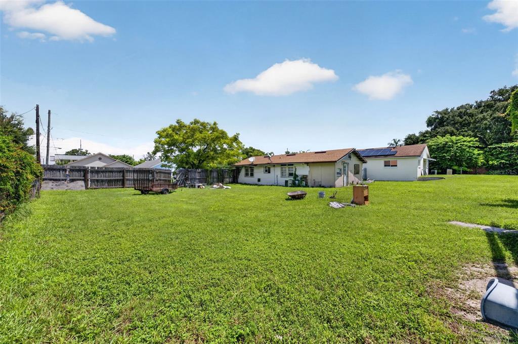A grassy backyard features a wooden fence, a small trailer, and two single-story houses — NEUSE AVENUE, ORLANDO, FL
