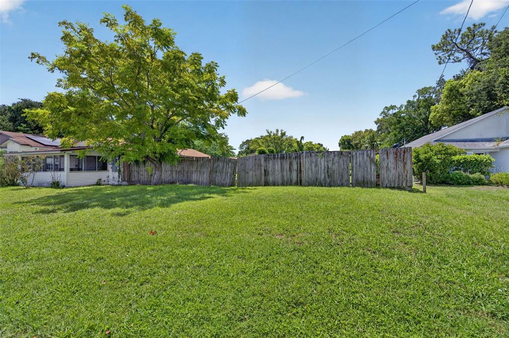 A grassy backyard features a wooden fence, a large tree, and adjacent residential houses — NEUSE AVENUE, ORLANDO, FL