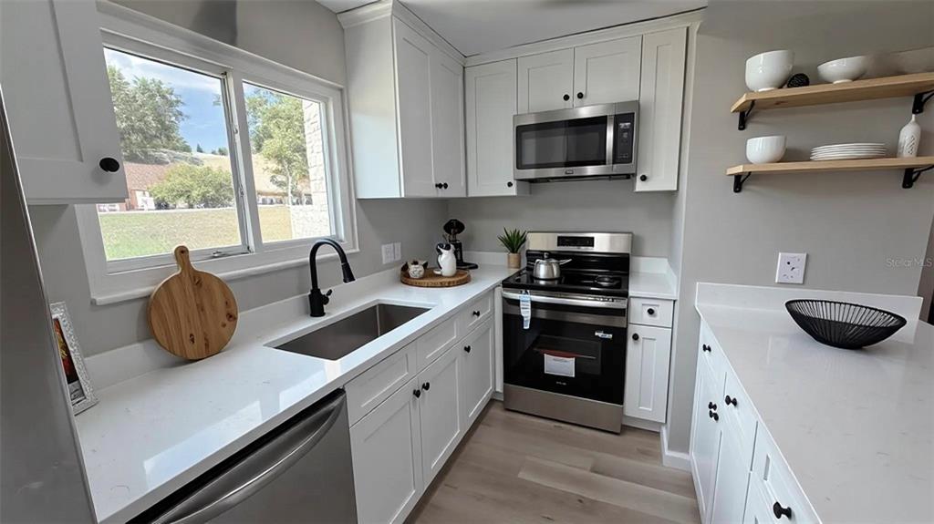 A modern kitchen features white cabinets, quartz countertops, stainless steel appliances, and open wood shelving — 434 SAND LIME ROAD, WINTER GARDEN, FL