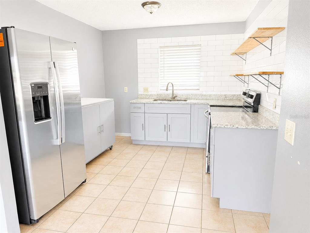 A kitchen with light gray cabinets, stainless steel appliances, granite countertops, and open wooden shelving — 1290 9TH STREET UNIT 108, DAYTONA BEACH, FL