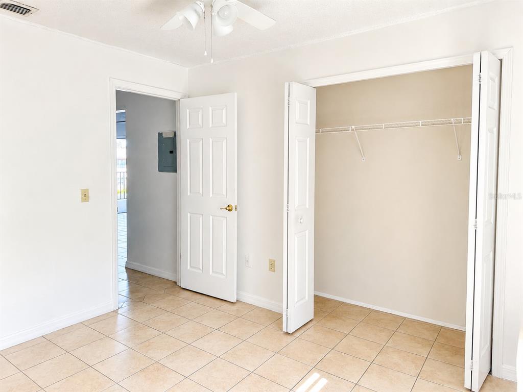 A room with beige tile flooring, a white door, and an open closet with shelving — 1290 9TH STREET UNIT 108, DAYTONA BEACH, FL