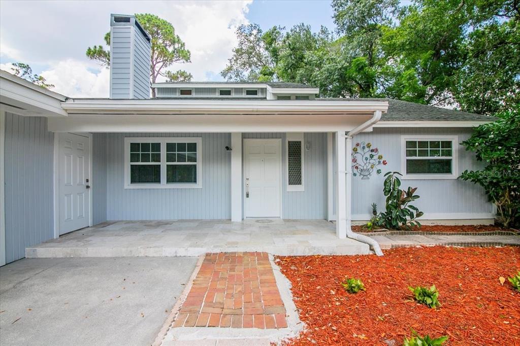 A light blue house exterior features a covered porch, brick walkway, and a white front door — 7147 LAGO STREET, SARASOTA, FL