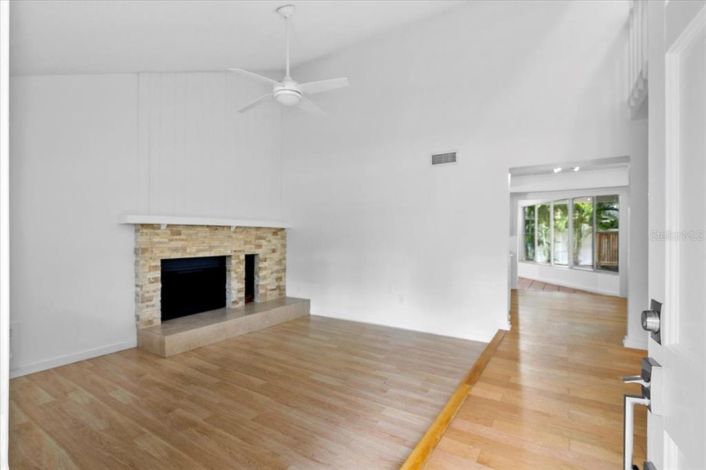 A living room with light wood flooring, a stone fireplace, and a vaulted ceiling — 7147 LAGO STREET, SARASOTA, FL