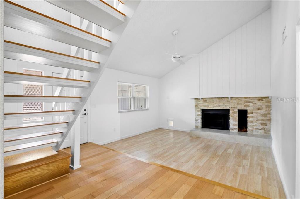 A living room features a stone fireplace, light wood flooring, and an open staircase — 7147 LAGO STREET, SARASOTA, FL