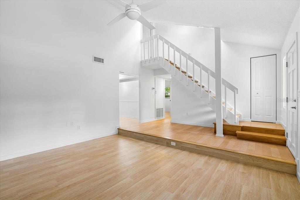 A living room with light wood flooring, a sunken floor area, and a white staircase — 7147 LAGO STREET, SARASOTA, FL