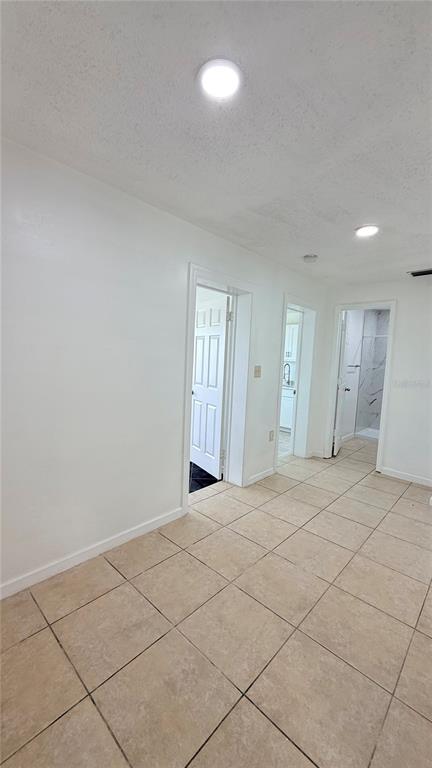 A room with beige tile flooring and white walls leads to two doorways and a bathroom — 1903 24TH UNIT B STREET, SARASOTA, FL