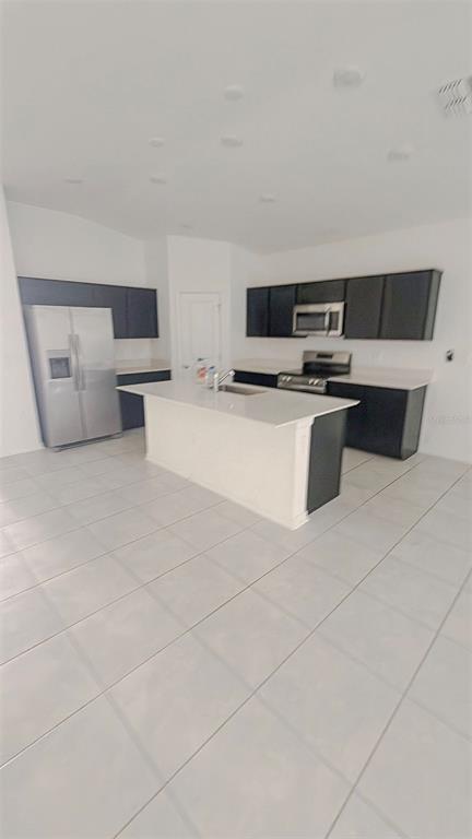 A kitchen features dark cabinetry, a white center island, stainless steel appliances, and tiled flooring — 652 REGGIE ROAD, WINTER HAVEN, FL