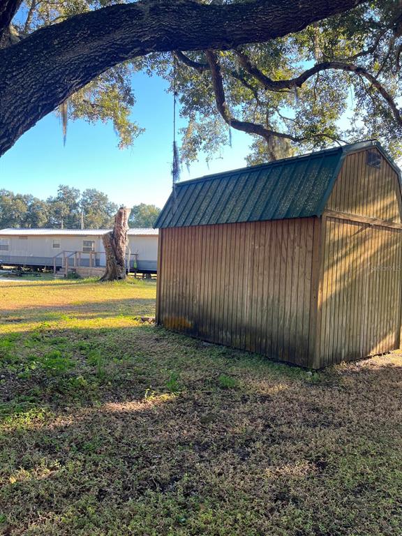 A wooden storage shed with a green metal roof sits under a large oak tree — 4015 SHADY OAK DRIVE E, LAKELAND, FL