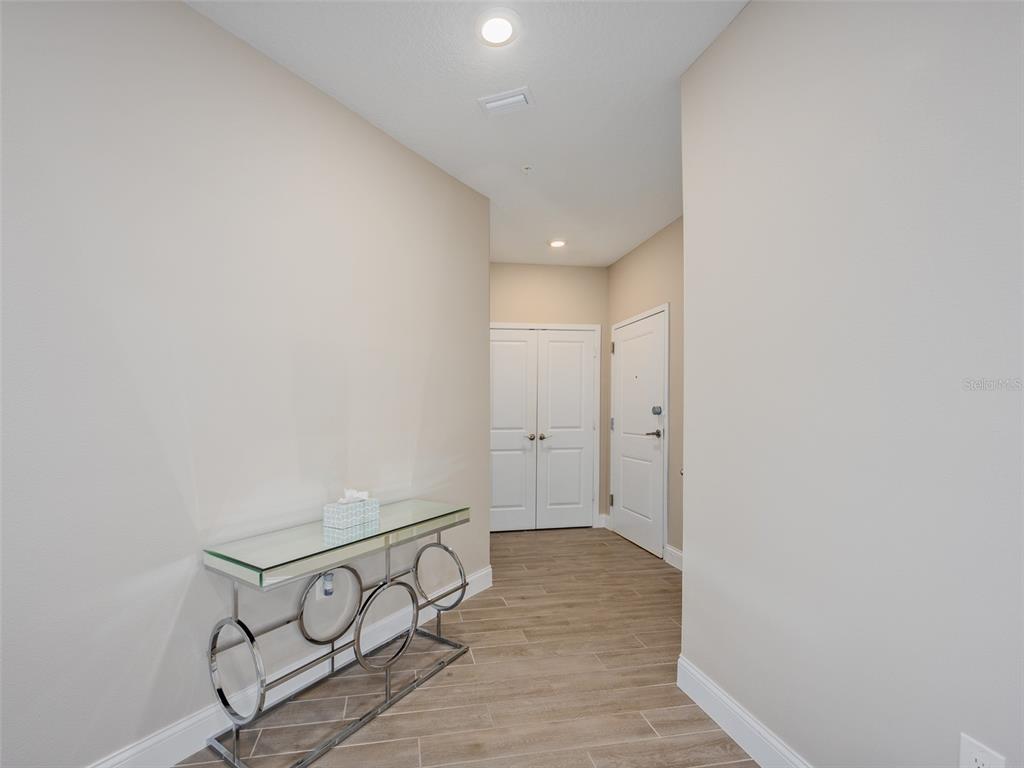 A hallway features light-colored walls, wood-look tile flooring, a glass console table, and two doors — 7517 LAUREATE BOULEVARD UNIT 4303, ORLANDO, FL