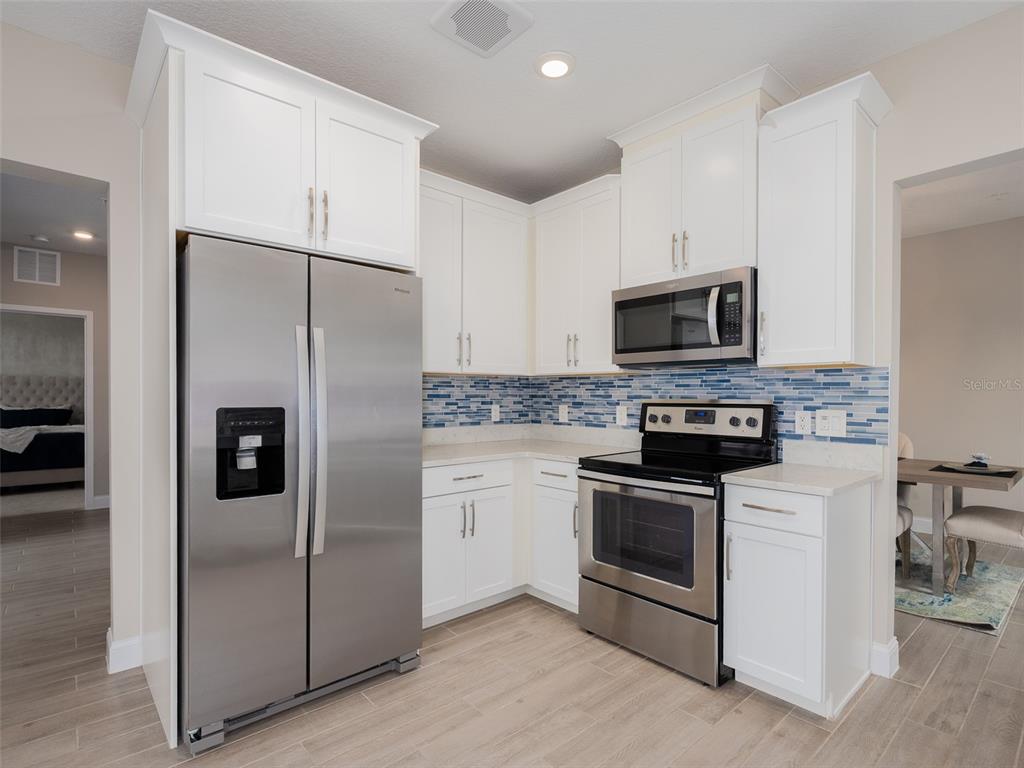A kitchen features white cabinets, stainless steel appliances, and a blue glass tile backsplash — 7517 LAUREATE BOULEVARD UNIT 4303, ORLANDO, FL