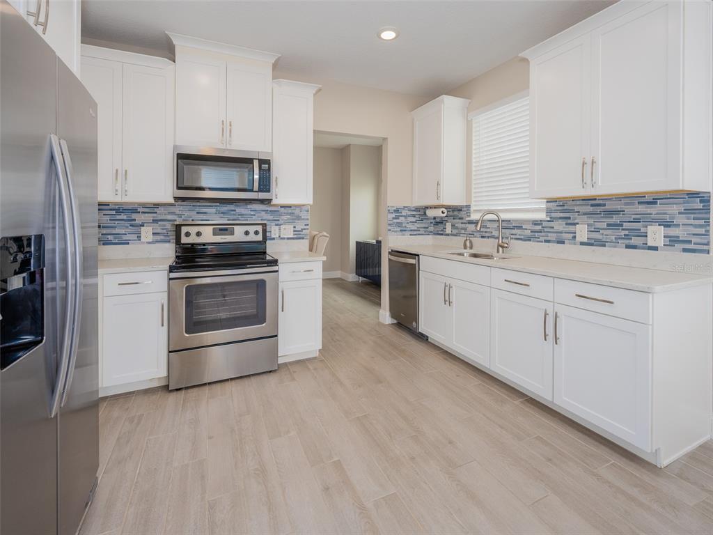 A modern kitchen features white cabinets, stainless steel appliances, and a blue glass tile backsplash — 7517 LAUREATE BOULEVARD UNIT 4303, ORLANDO, FL