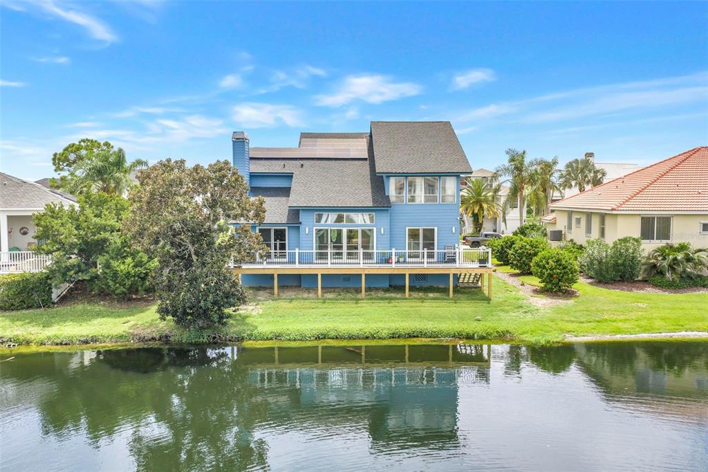 A blue two-story house with a wooden deck sits beside a calm lake — 2111 HARBOUR WATCH DRIVE, TARPON SPRINGS, FL