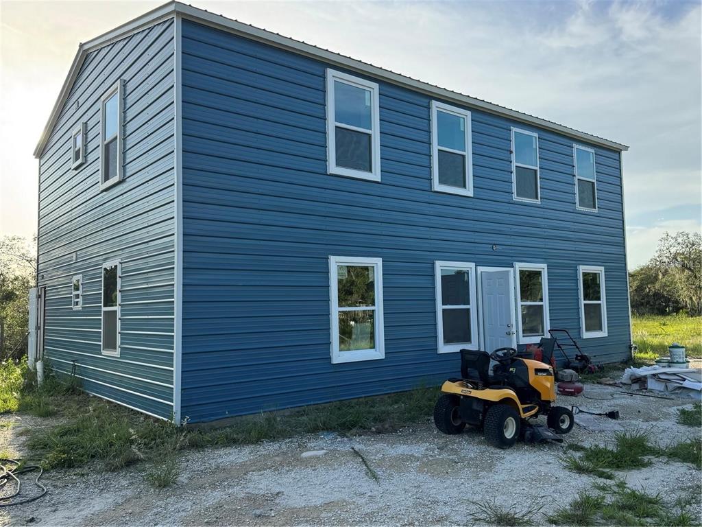 A two-story blue metal-sided building with multiple windows and a yellow lawn tractor parked outside — 206 BRANDYWINE TRAIL, FROSTPROOF, FL