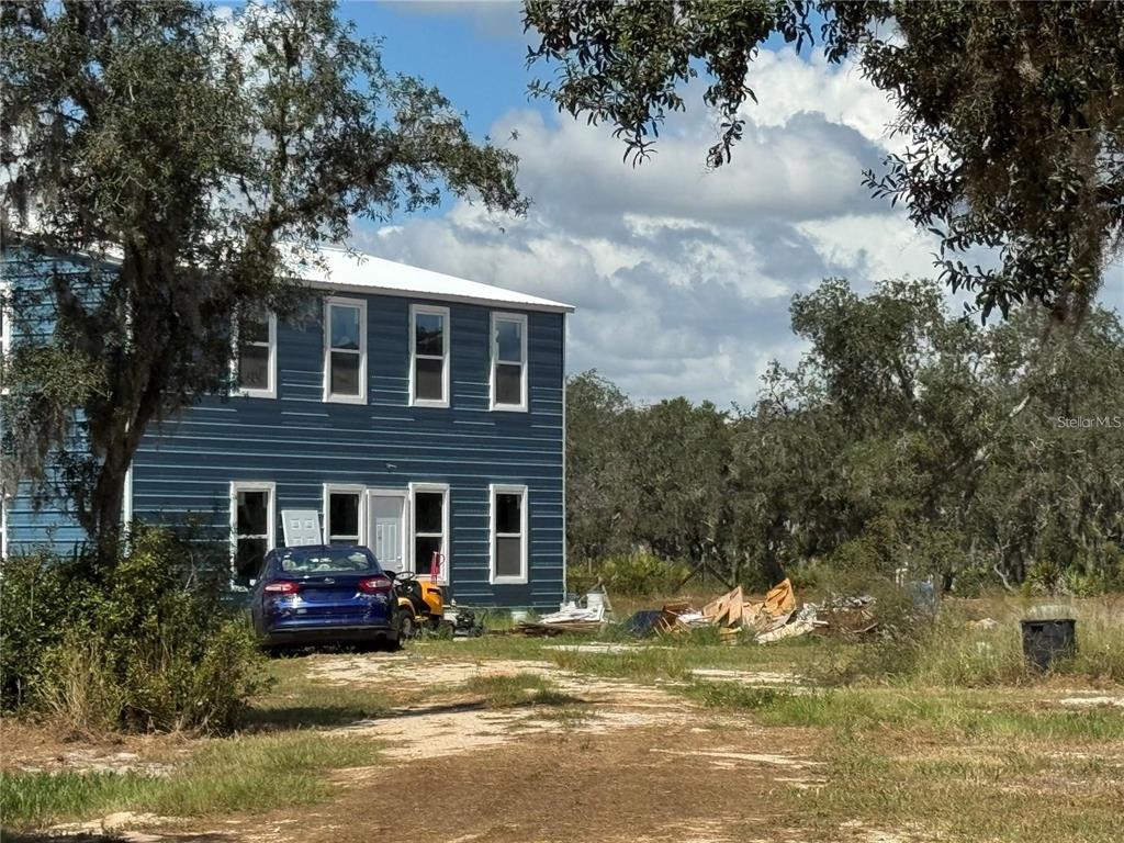 A two-story blue house with a metal roof sits on a dirt lot with debris — 206 BRANDYWINE TRAIL, FROSTPROOF, FL