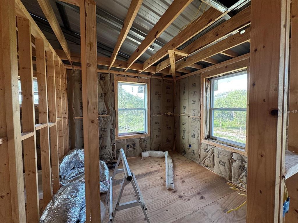 An unfinished room with exposed wood framing, fiberglass insulation, and two windows — 206 BRANDYWINE TRAIL, FROSTPROOF, FL