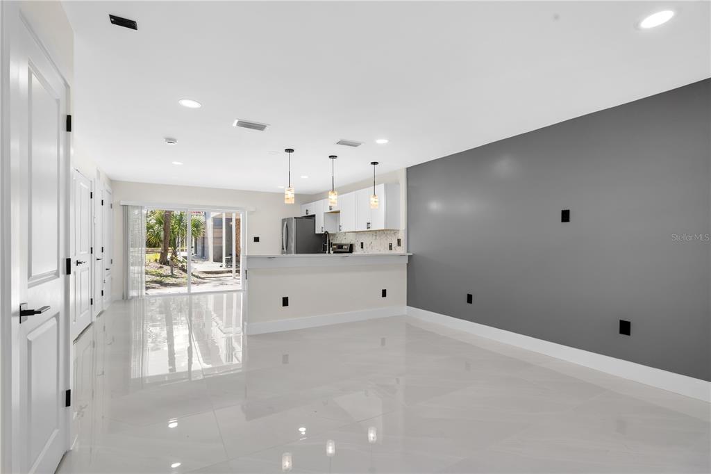 A bright, open-concept living area features white tile floors, a gray accent wall, and kitchen — 7300 DANIEL WEBSTER DRIVE UNIT M7, WINTER PARK, FL