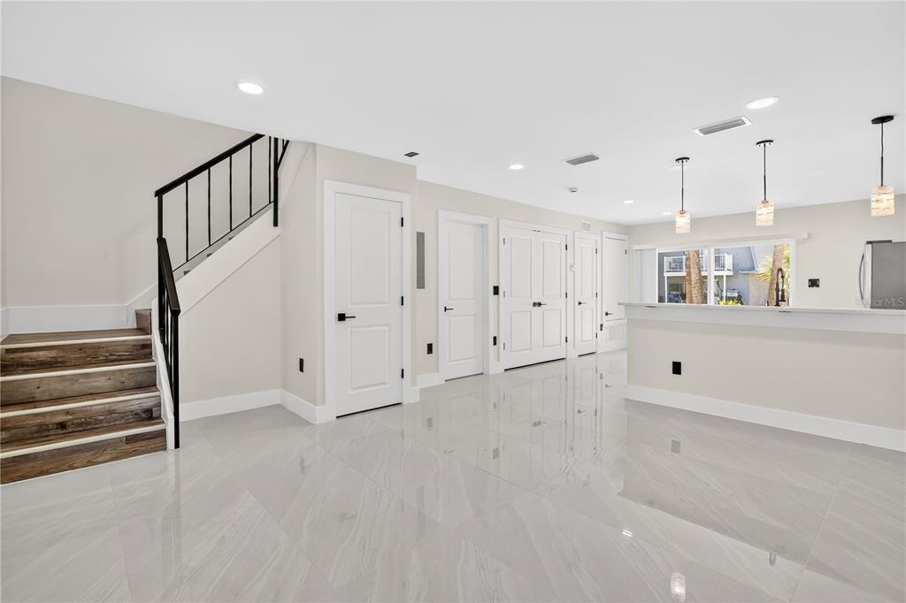 A bright, open-concept living area features white tile flooring, a staircase with black railings, and a kitchen — 7300 DANIEL WEBSTER DRIVE UNIT M7, WINTER PARK, FL