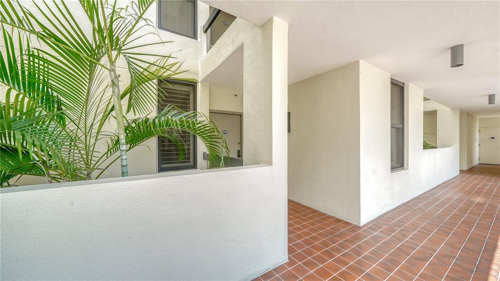 A tiled outdoor walkway leads to a building entrance with a large potted palm tree — 1930 HARBOURSIDE DRIVE UNIT 122, LONGBOAT KEY, FL