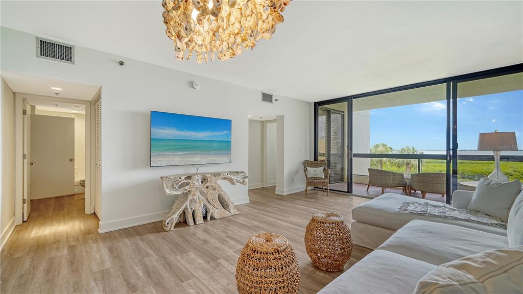 A living room features light wood flooring, a driftwood console, and a balcony with water views — 1930 HARBOURSIDE DRIVE UNIT 122, LONGBOAT KEY, FL
