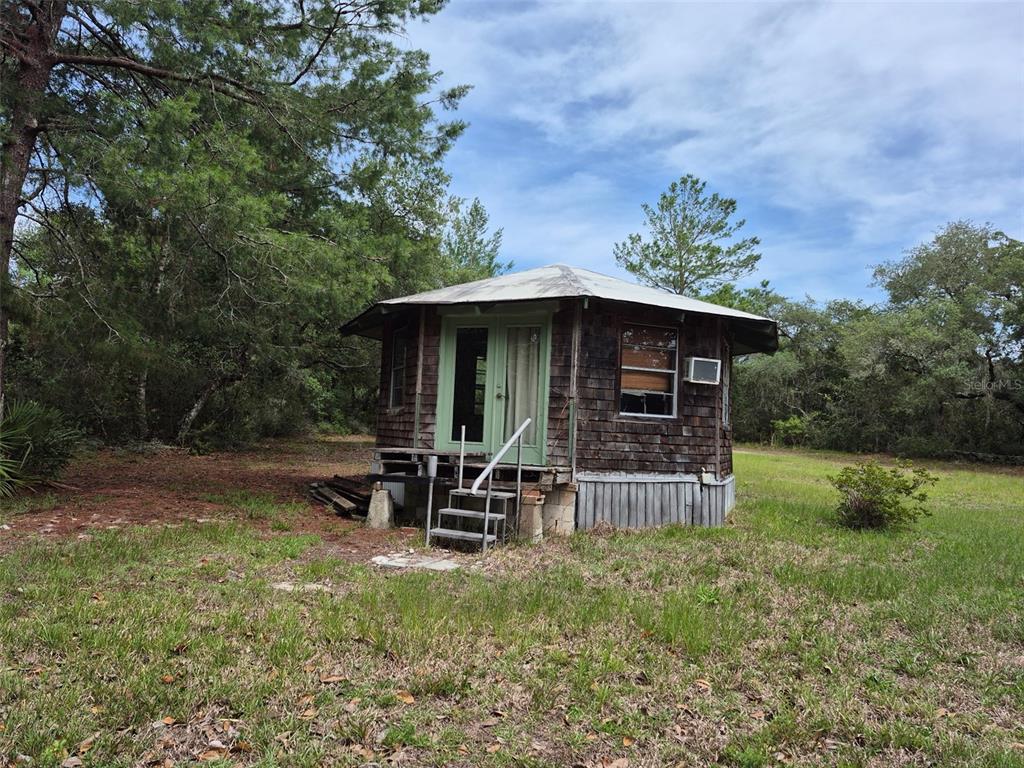 A small, weathered wooden cabin with a metal roof sits on a grassy lot — 15764 NE 235TH PLACE, FORT MC COY, FL