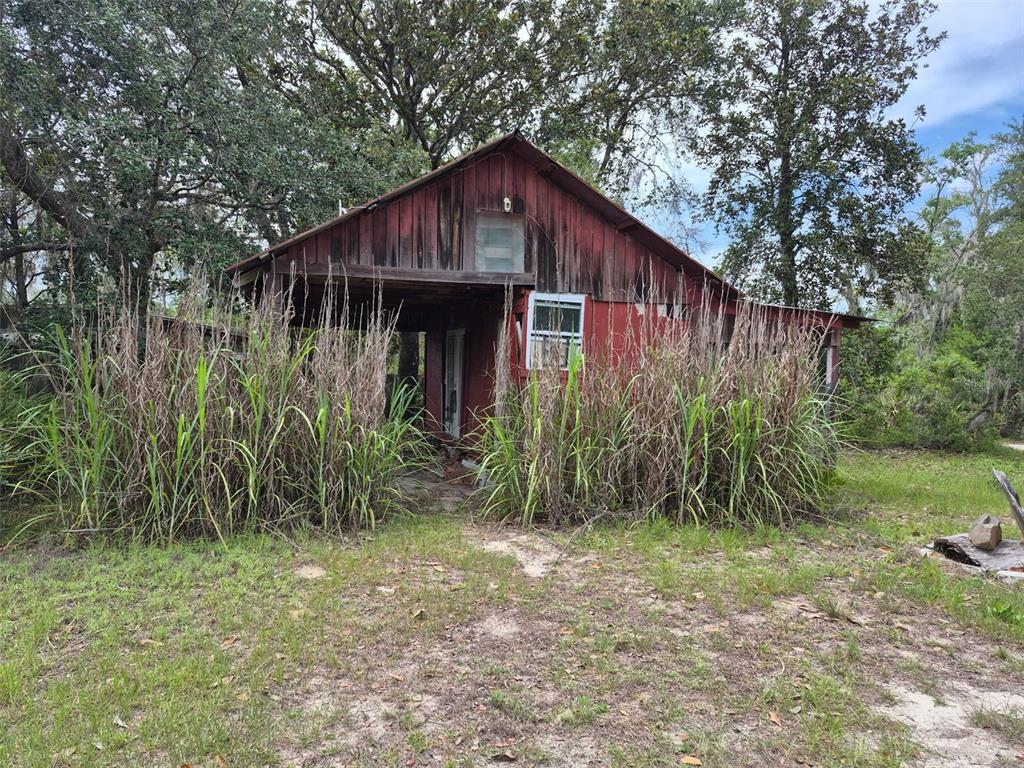 A weathered red wooden cabin stands surrounded by tall grass and mature trees — 15764 NE 235TH PLACE, FORT MC COY, FL