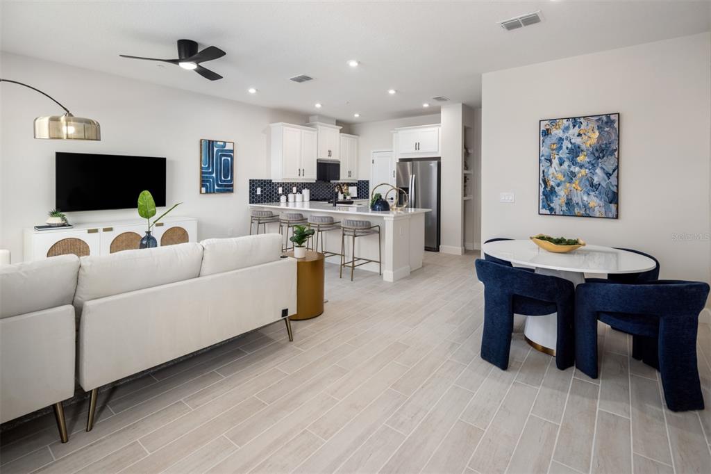 An open-concept living room, kitchen, and dining area featuring white cabinetry and light tile flooring — 2844 CAMELLIA FLOWER STREET, APOPKA, FL