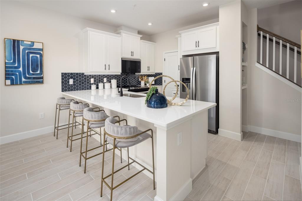 A modern kitchen features white cabinets, a quartz island with bar seating, and blue tile backsplash — 2844 CAMELLIA FLOWER STREET, APOPKA, FL