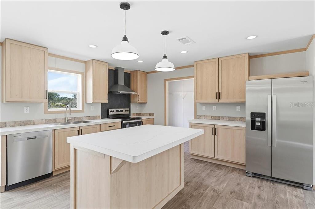 A kitchen features light wood cabinets, stainless steel appliances, a center island, and white countertops — 4510 CROWS BLUFF AVENUE, LAKE WALES, FL