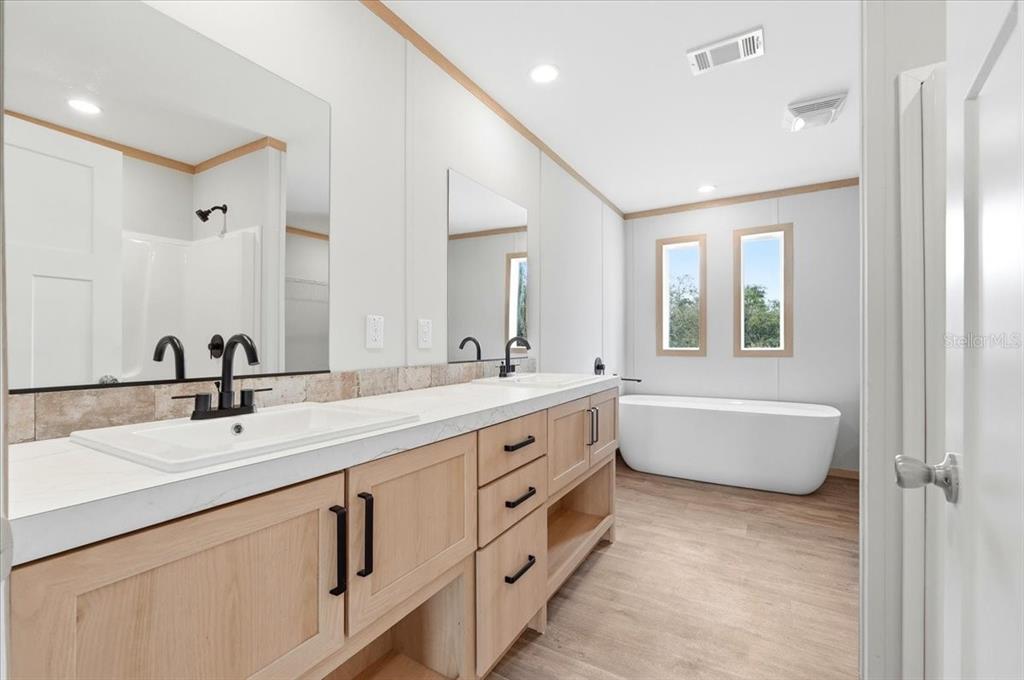 A bathroom features a double vanity with light wood cabinets and a freestanding soaking tub — 4510 CROWS BLUFF AVENUE, LAKE WALES, FL