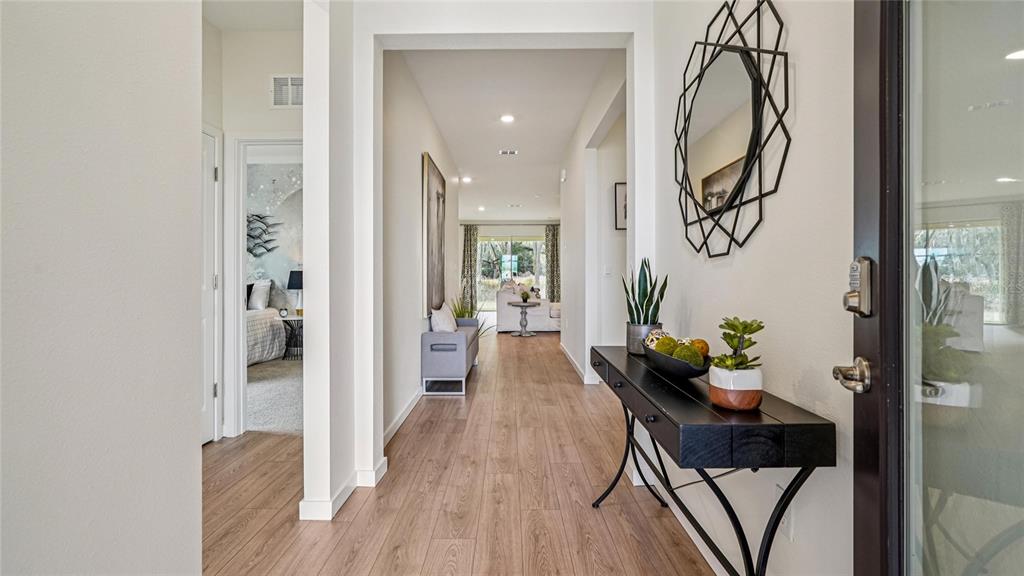 A bright entryway features wood-look flooring, a black console table, and a geometric wall mirror — 4555 NW 39TH STREET ROAD, OCALA, FL