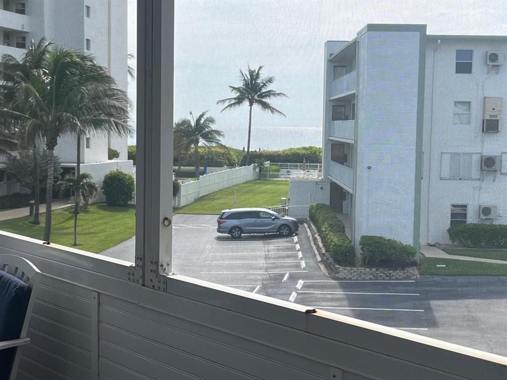 A view from a screened balcony overlooking a parking lot, palm trees, and the ocean — 3600 N OCEAN DRIVE UNIT 310, RIVIERA BEACH, FL