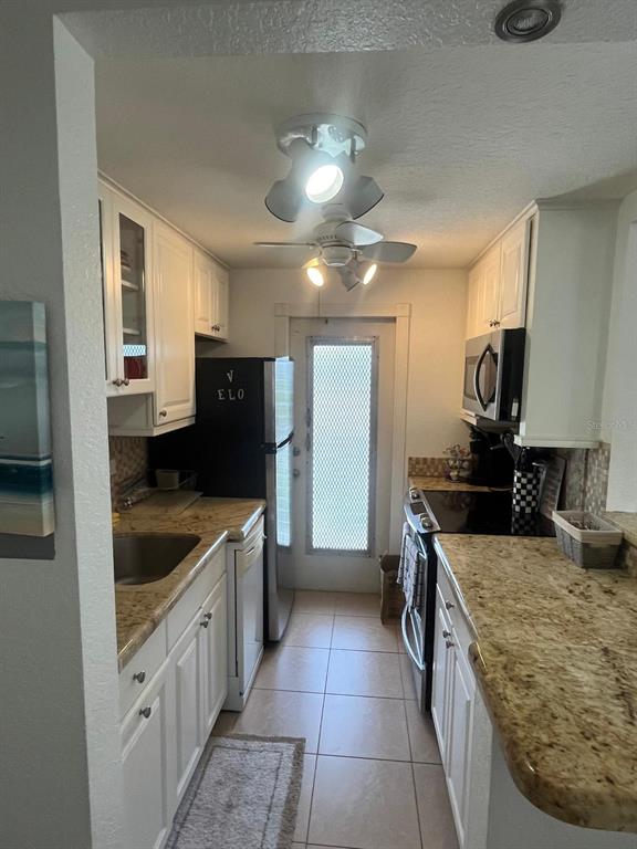 A galley kitchen features white cabinets, granite countertops, stainless steel appliances, and a ceiling fan — 3600 N OCEAN DRIVE UNIT 310, RIVIERA BEACH, FL