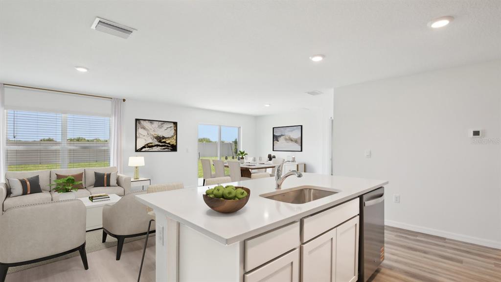 This open-concept kitchen and living area features a central island, light cabinetry, and wood-look flooring — 1134 BOURBON AVENUE, PARRISH, FL