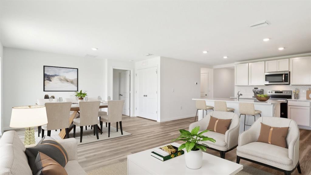 An open-concept living and dining area features light wood flooring, white cabinetry, and neutral furniture — 1134 BOURBON AVENUE, PARRISH, FL