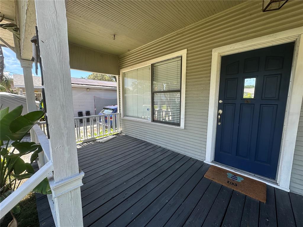 A covered front porch features dark wooden decking, a blue front door, and light siding — 1308 E FRIERSON AVENUE, TAMPA, FL