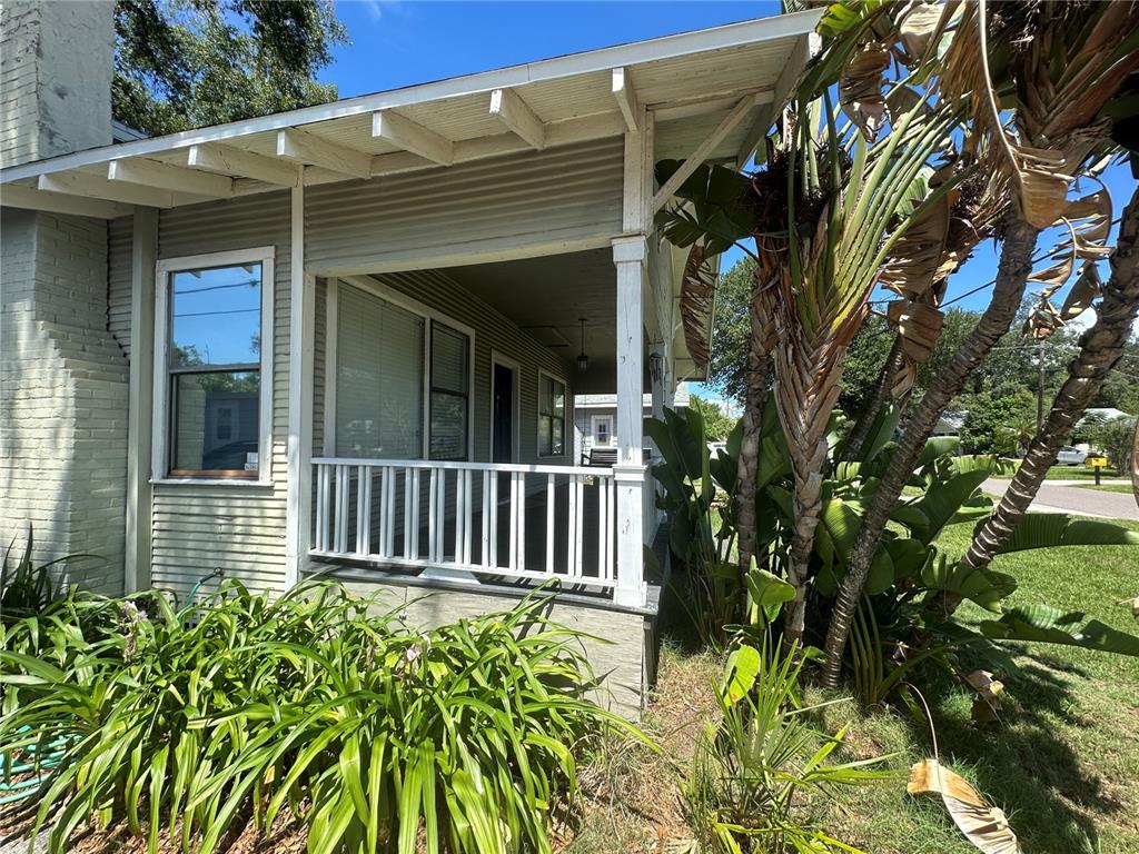 A covered front porch with a white railing sits beside a house with light-colored siding — 1308 E FRIERSON AVENUE, TAMPA, FL