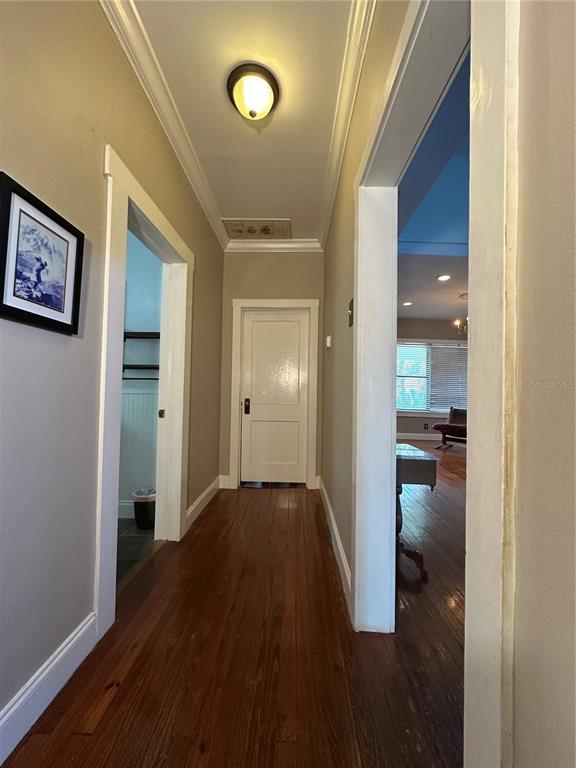 A hallway with hardwood floors leads to a white door and an adjacent living area — 1308 E FRIERSON AVENUE, TAMPA, FL