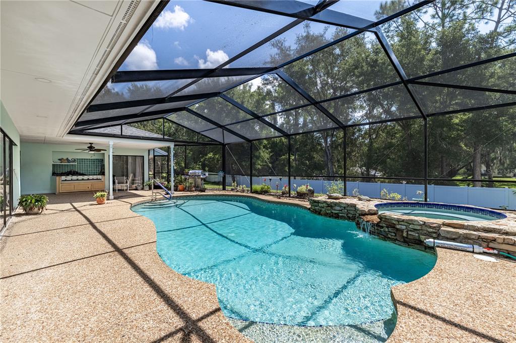 A screened-in pool area features a stone-accented hot tub with a waterfall and pebble decking — 33816 SPRING DRIVE, LEESBURG, FL