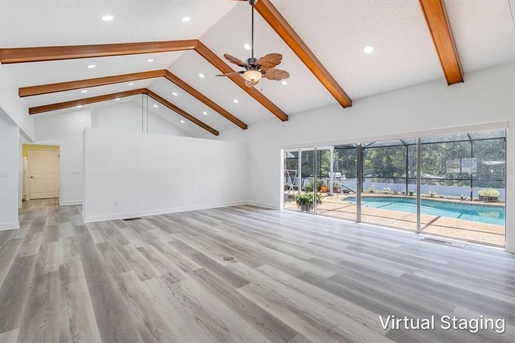 An empty living room with vaulted ceilings, wood beams, light wood flooring, and pool views — 33816 SPRING DRIVE, LEESBURG, FL