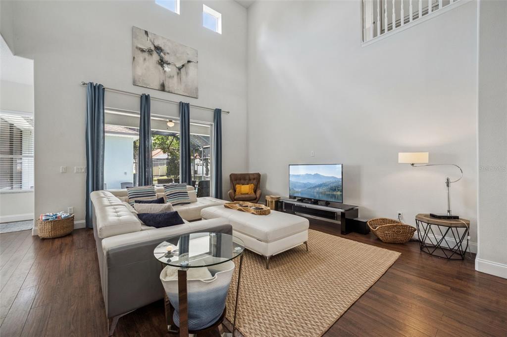 A living room features high ceilings, a white sectional sofa, and dark wood flooring — 7412 DEVEREAUX STREET, REUNION, FL