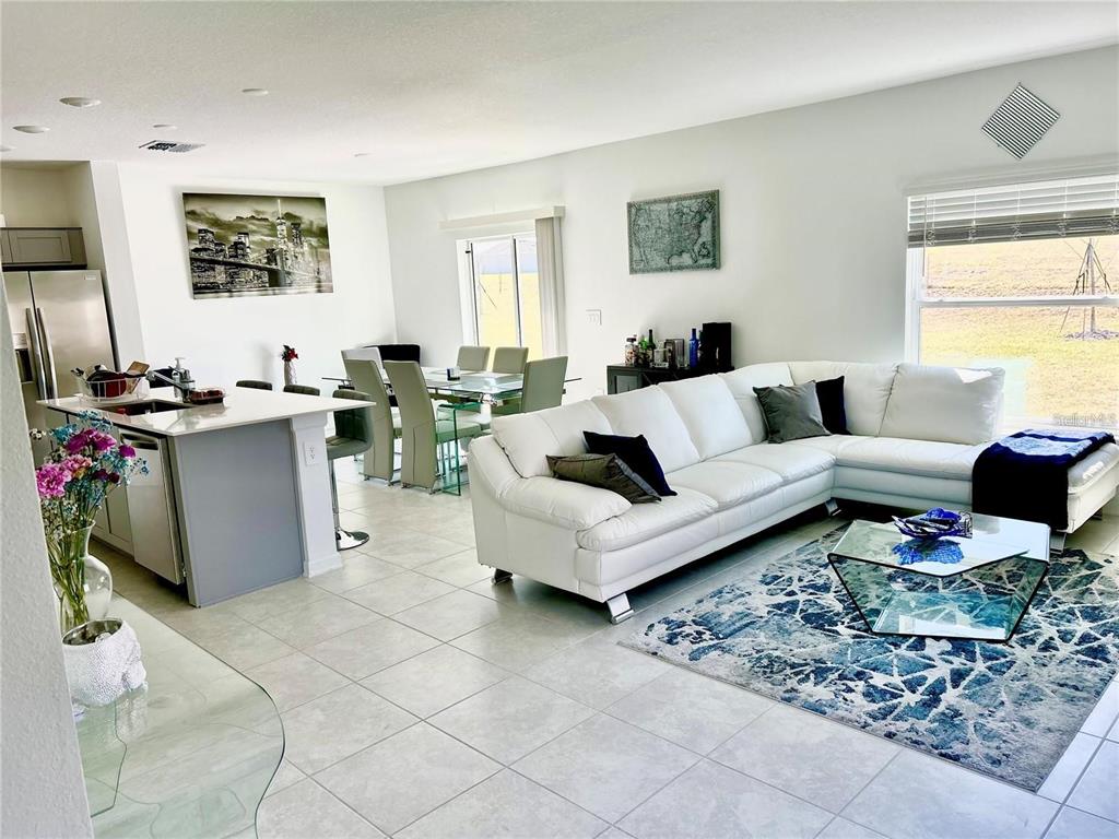An open-concept living and dining area features white tile floors, a white sectional, and kitchen — 572 REGGIE ROAD, WINTER HAVEN, FL