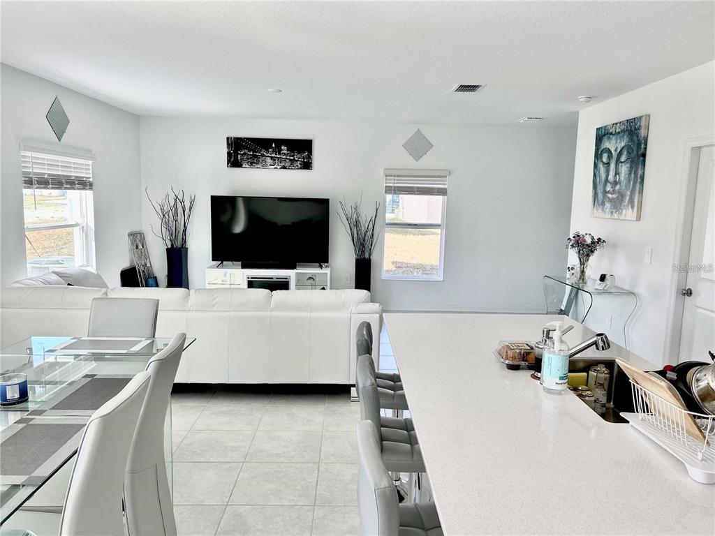 A bright open-concept living room and kitchen area with white furniture and tile flooring — 572 REGGIE ROAD, WINTER HAVEN, FL